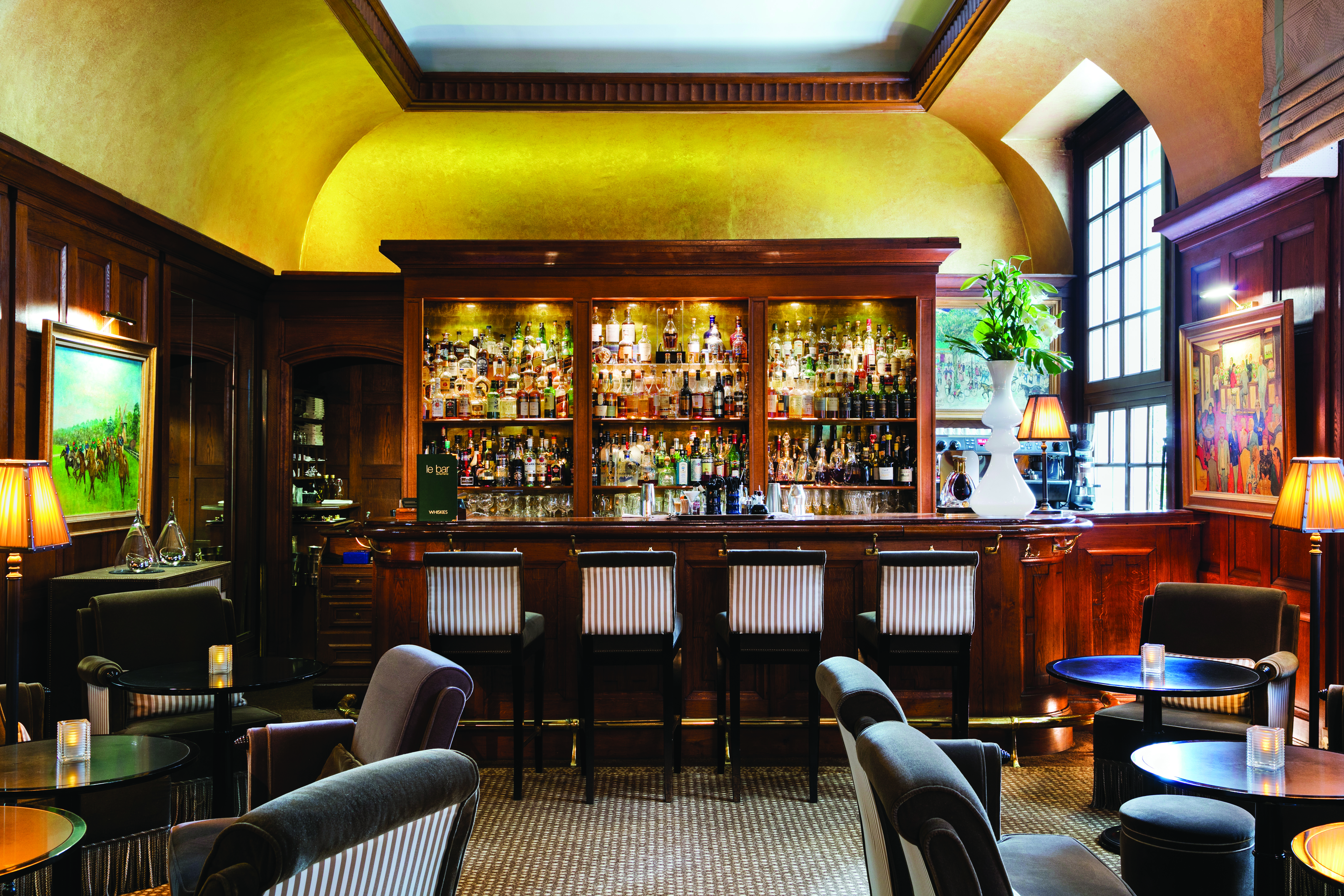 Bar with seating areas, a wooden bar with a cabinet of drinks behind and wooden bar stools to sit on 