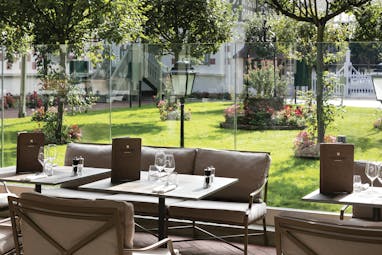 Outdoor terrace dining area at the Hotel Normandy Barriere with tables laid out overlooking green grass and trees