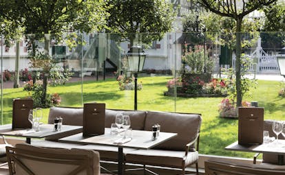 Outdoor terrace dining area at the Hotel Normandy Barriere with tables laid out overlooking green grass and trees