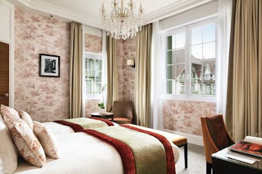 Twin room with two single beds, pink, red and beige colour scheme and two large windows with a glass chandelier hanging from the ceiling