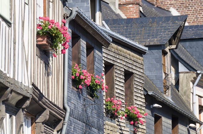 Rustic grey and brown houses with pink flowers in windowboxes in Honfleur