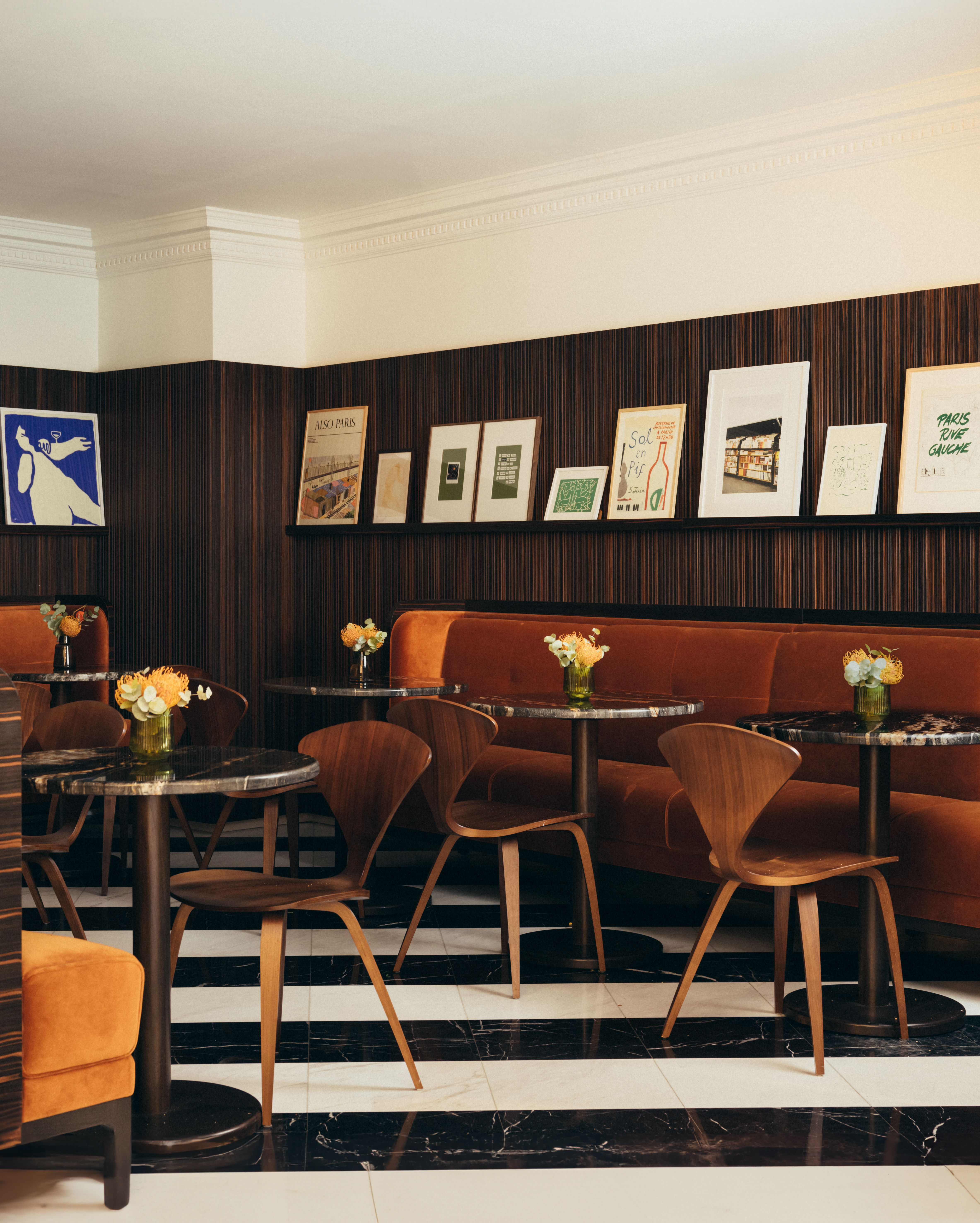 Hotel Bourgogne et Montana breakfast room, with wood panelled walls, shelves of framed artwork and posters, and burnt orange booth with shell-like wooden chairs