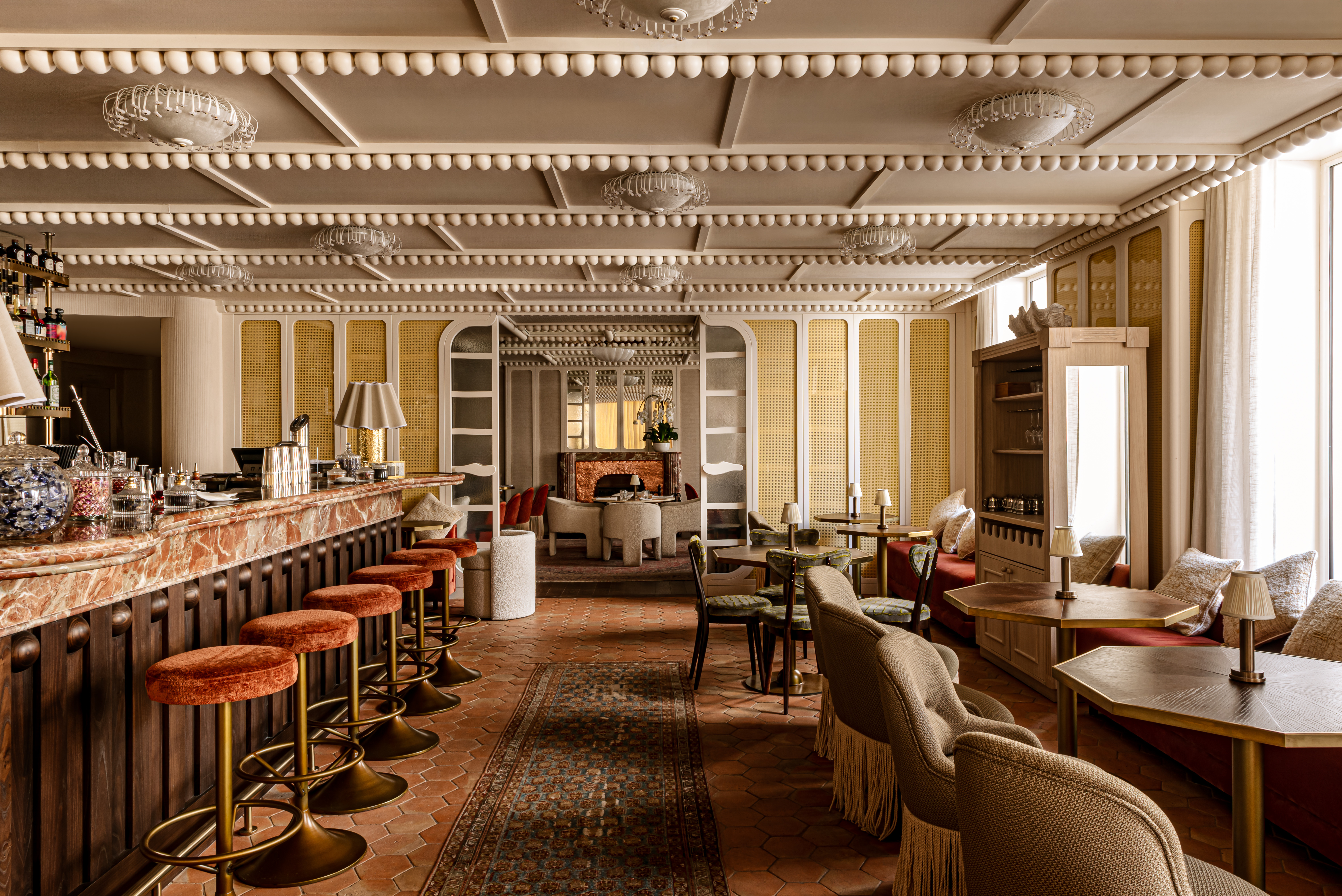 Chateau des Fleurs restaurant with vintage style furnishings in neutral tones with splashes of rich red in the bar stools, and a decorative ceiling and floor-to-ceiling windows