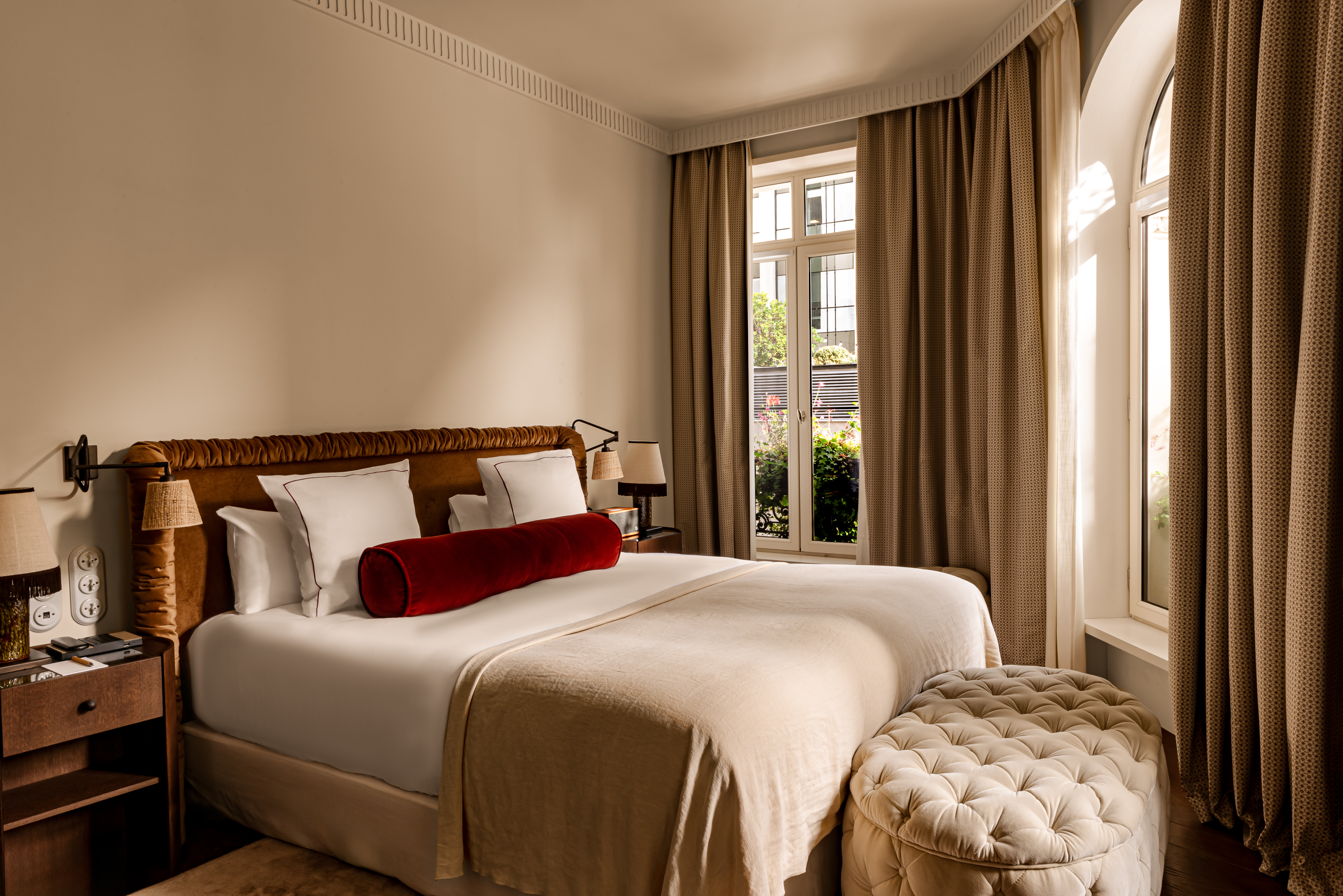 Chateau des Fleurs guestroom with large corner windows, double bed, and classic, neutral colour palette with rich red cushions