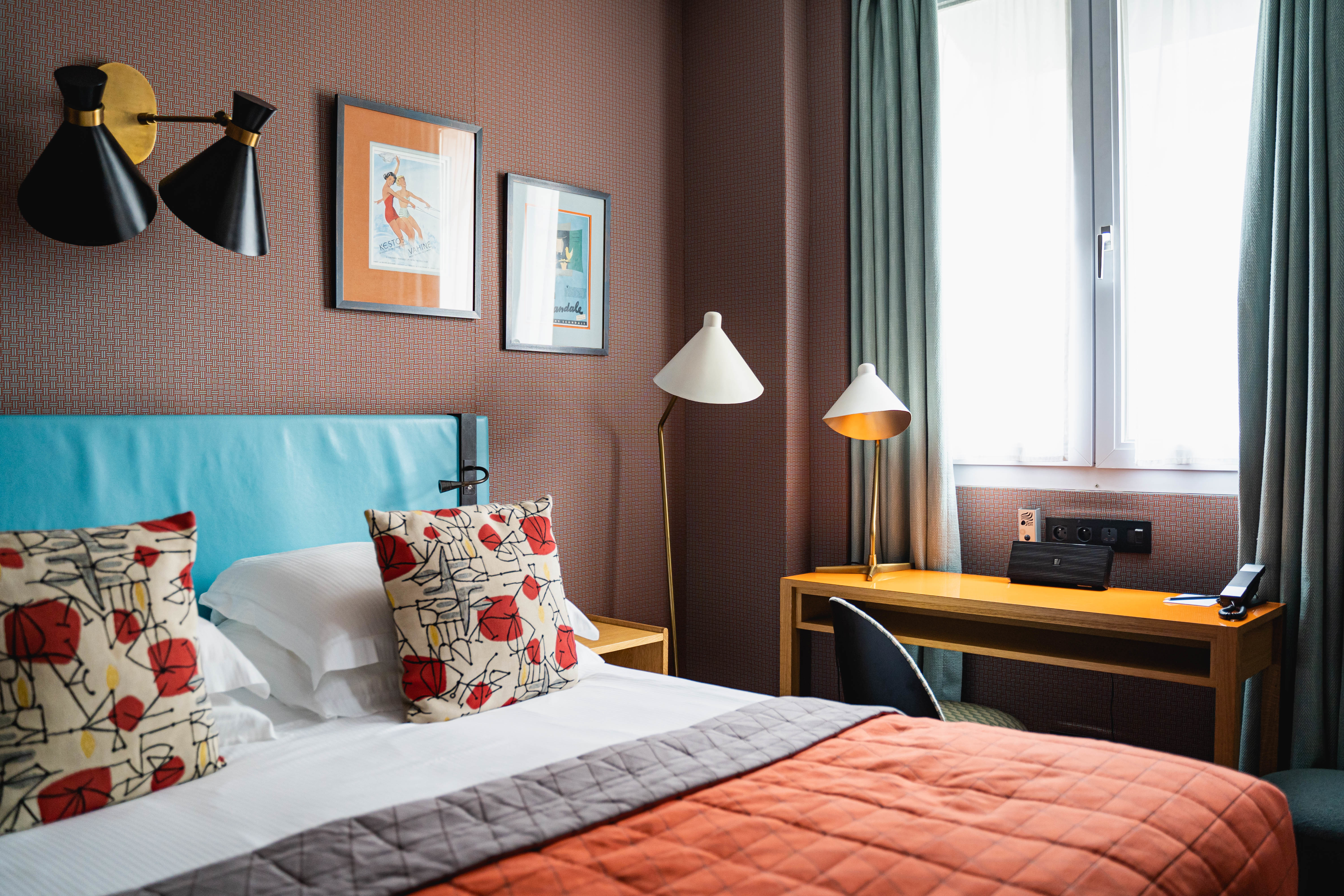 Hotel Artus Classic room with orange, blue, and mauve decor, floral cushions, light double window, and 1950s inspired lamps