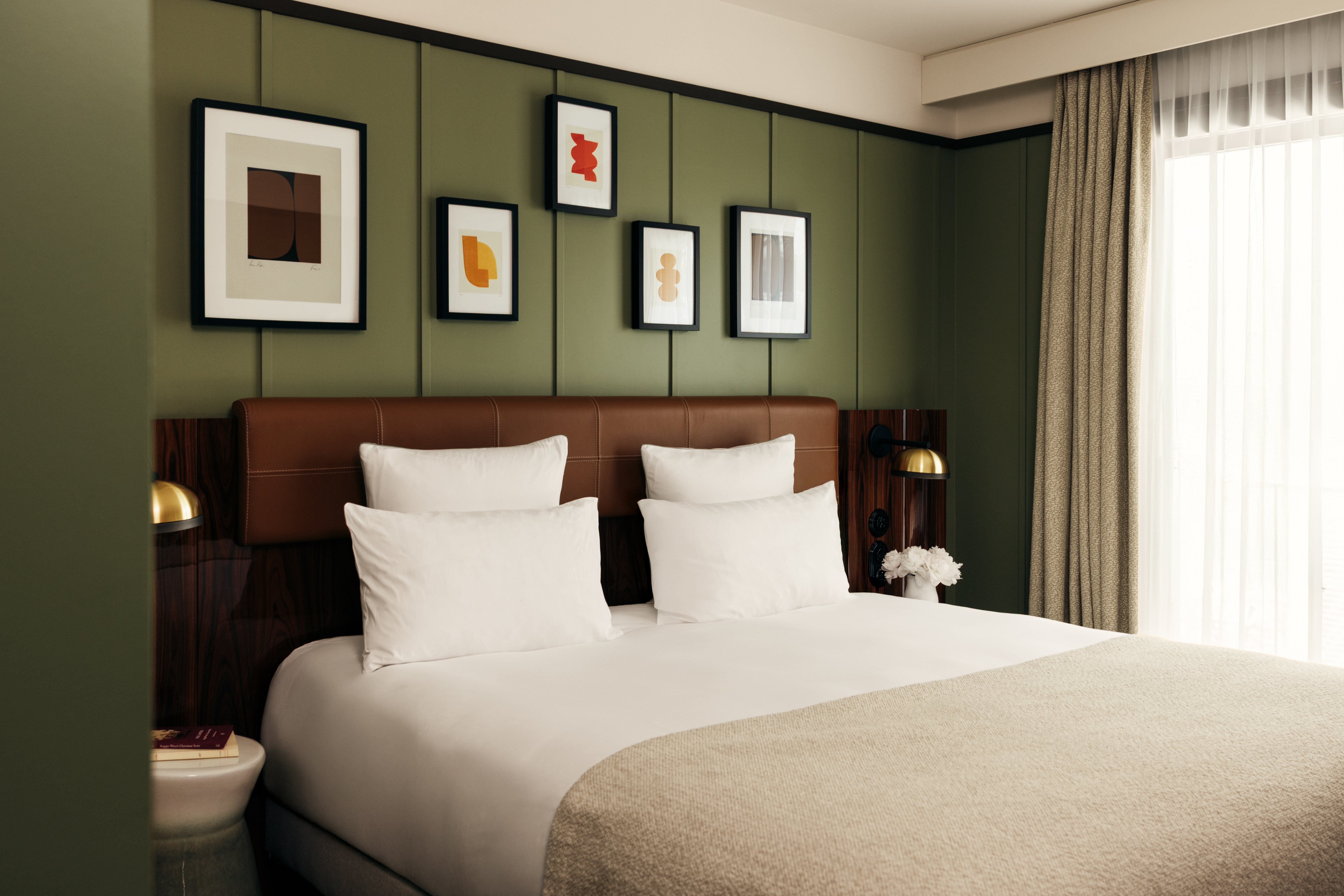 Hotel Norman Cozy Room with dark green panelled walls, cream bed linen and small abstract artworks on the walls