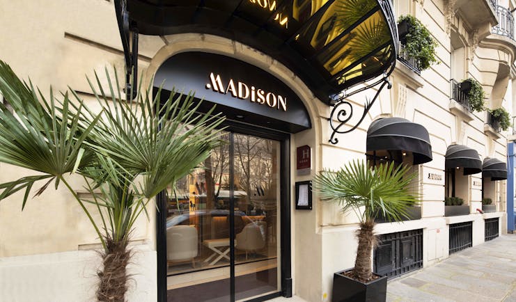 Grand door with awning and palm tree plants outside on pavement at the Madison Hotel Paris