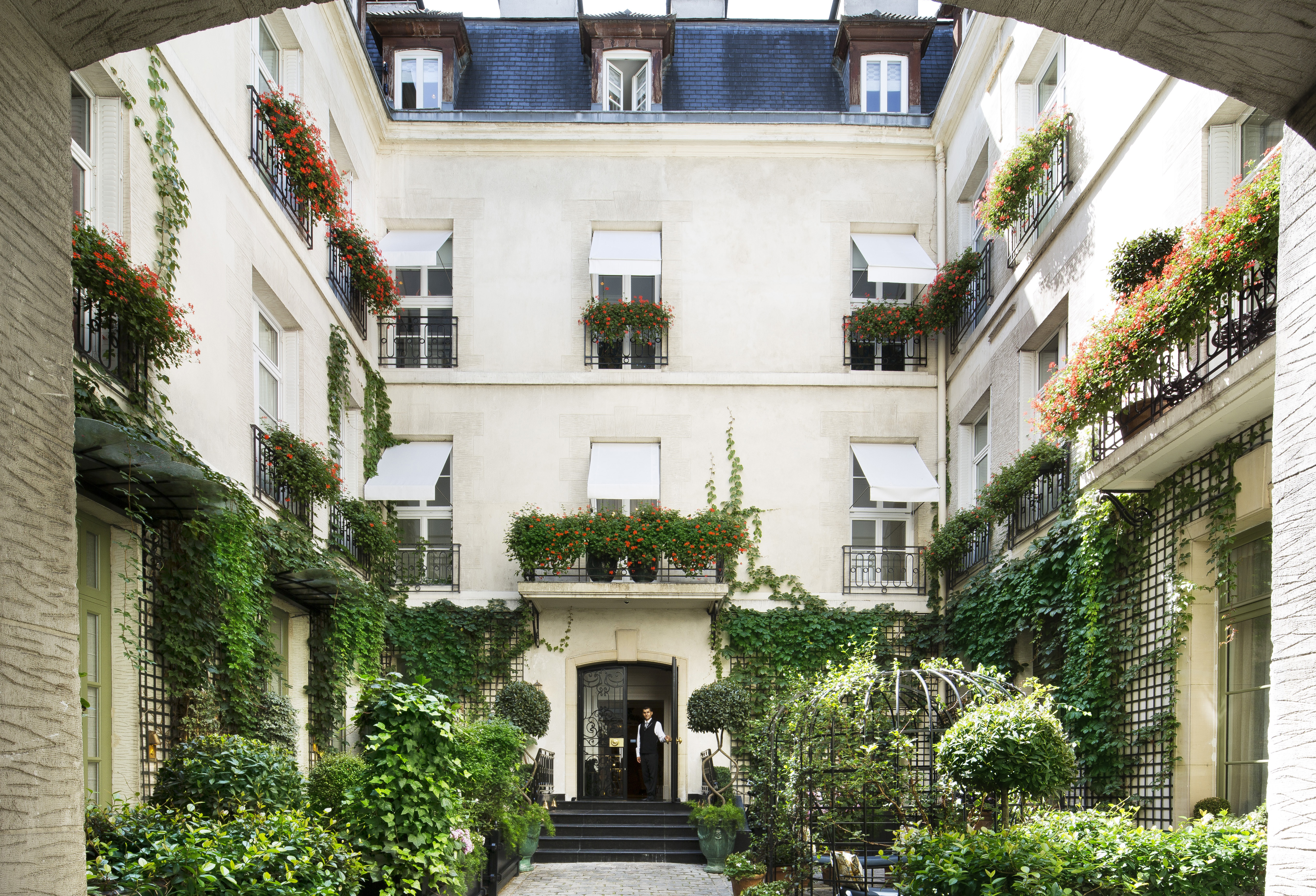 Relais Christine Paris courtyard with plants and exterior with white shutters at windows