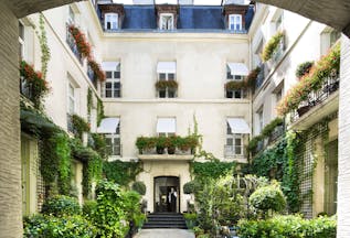 Relais Christine Paris courtyard with plants and exterior with white shutters at windows