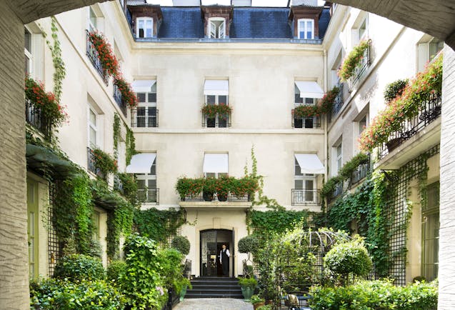 Relais Christine Paris courtyard with plants and exterior with white shutters at windows