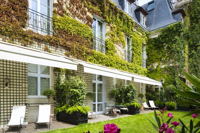 Private garden with vines growing up the hotel building and sun loungers on the lawn 