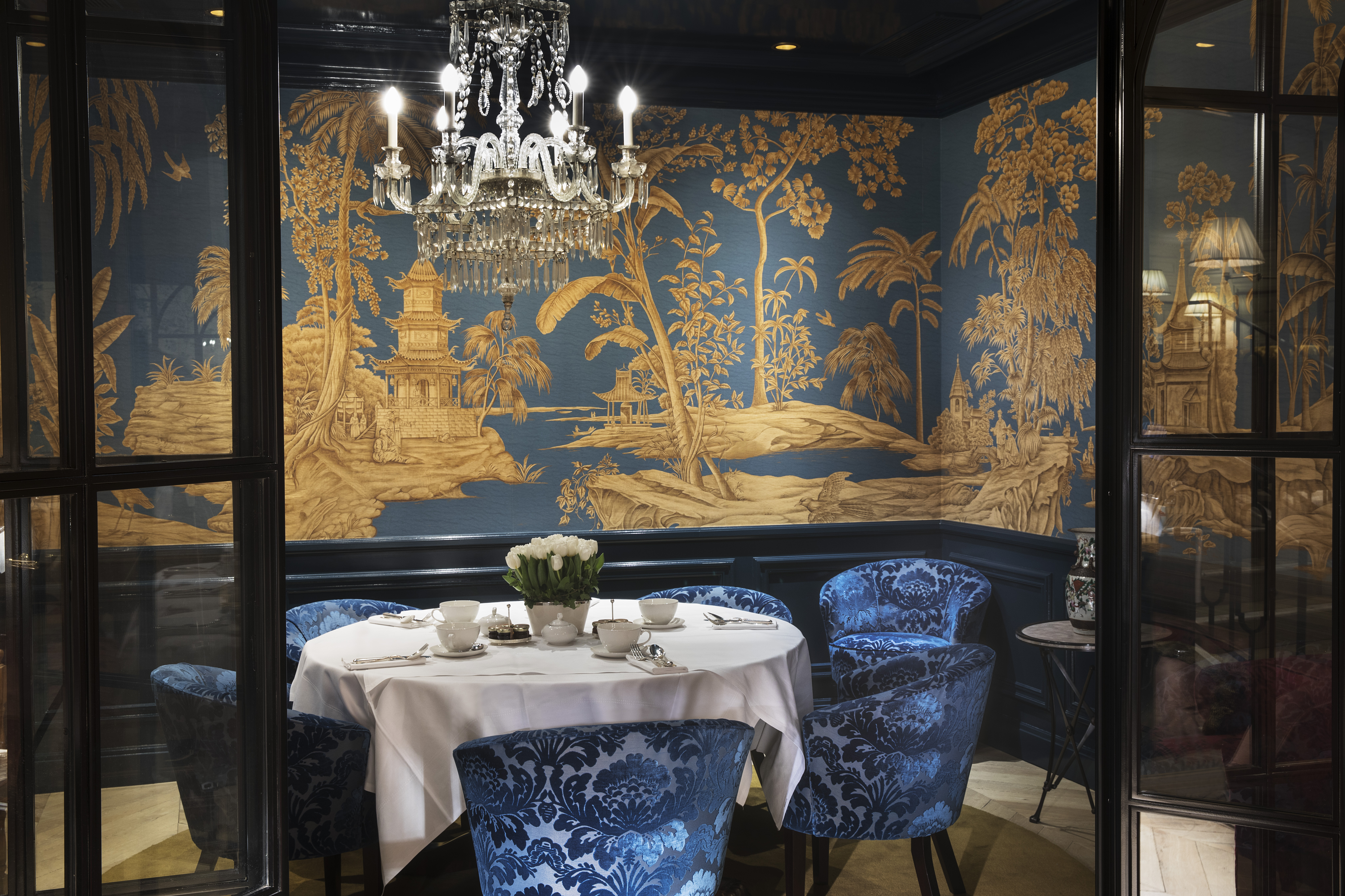 Restaurant with table set up for dining with chandelier and blue velvet chairs 