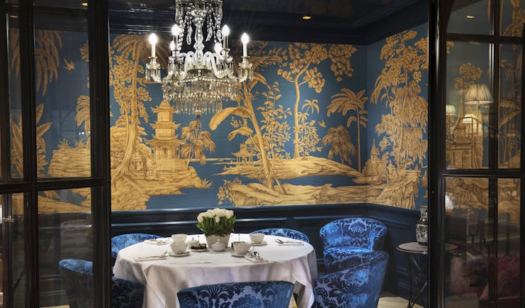 Restaurant with table set up for dining with chandelier and blue velvet chairs 