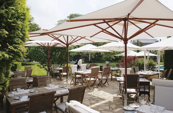 Outdoor dining area with tables and chairs set out on a terrace and white umrbellas shading them