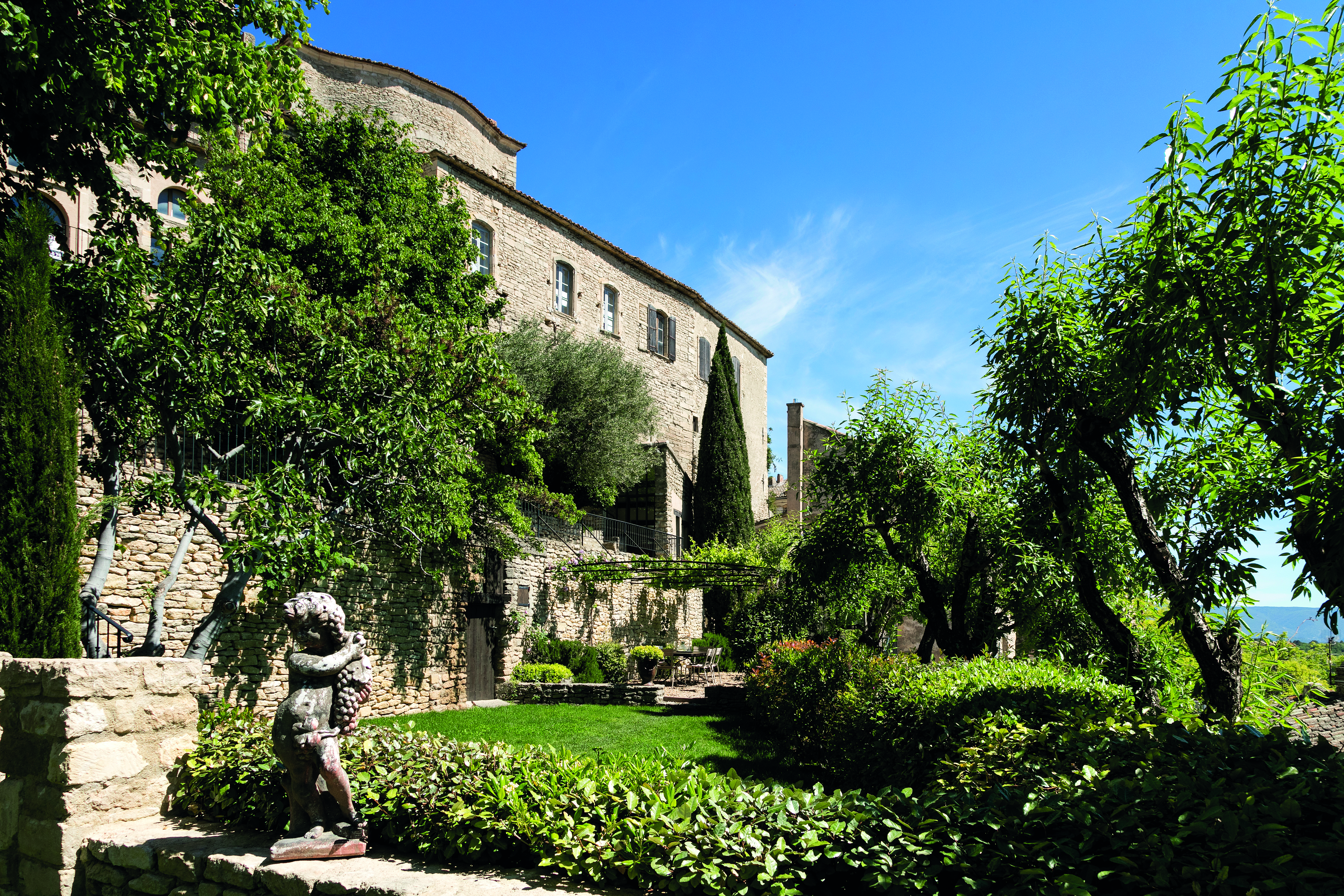 La Bastide de Gordes Provence exterior sculpture stone building garden trees and a sculpture of a young boy with grapes