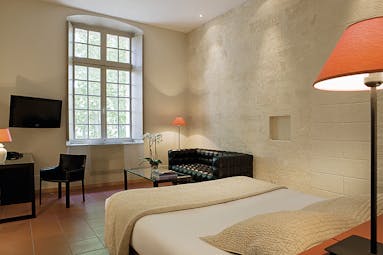 Le Cloitre Saint Louis Avignon bedroom with stone walls black sofa television and desk