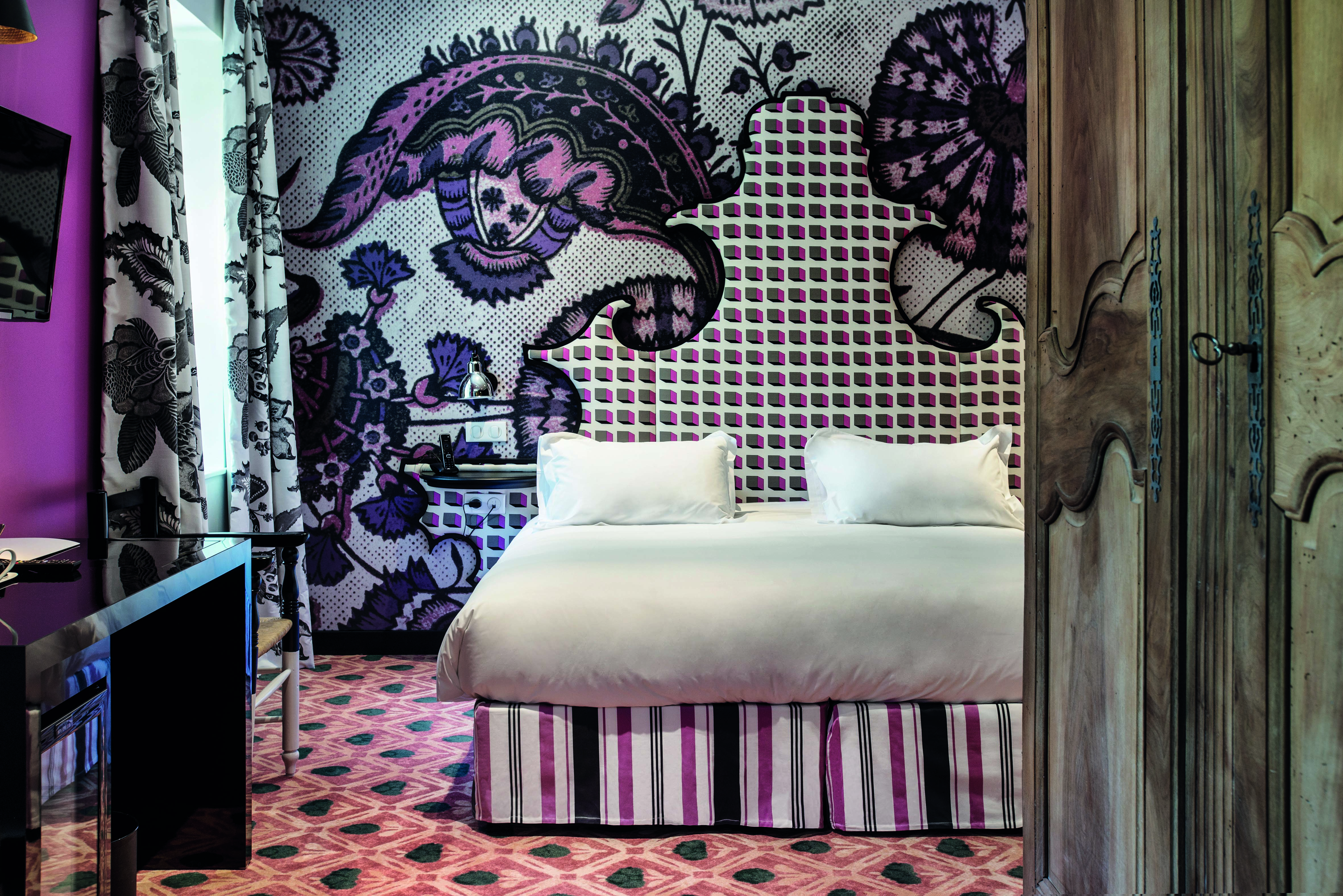 Hotel Jules Cesar Provence bedroom with one bright pink wall and one wall with graphic print patterned carpet