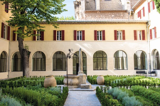 Hotel Jules Cesar Provence exterior courtyard surrounded by a building with large windows topiary and statues