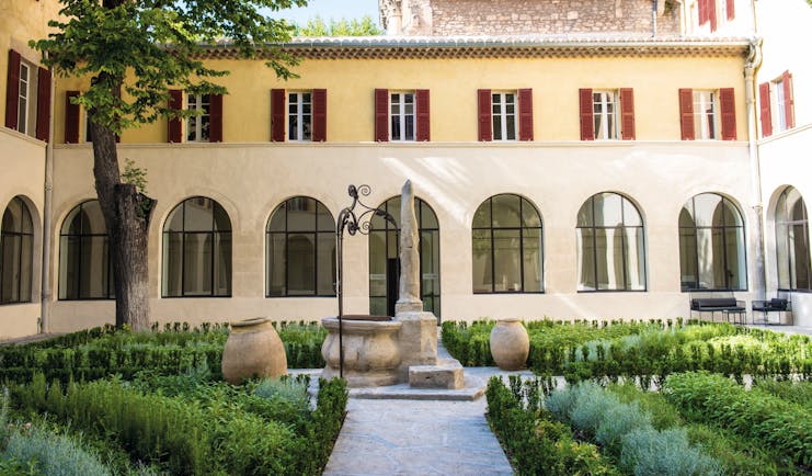 Hotel Jules Cesar Provence exterior courtyard surrounded by a building with large windows topiary and statues