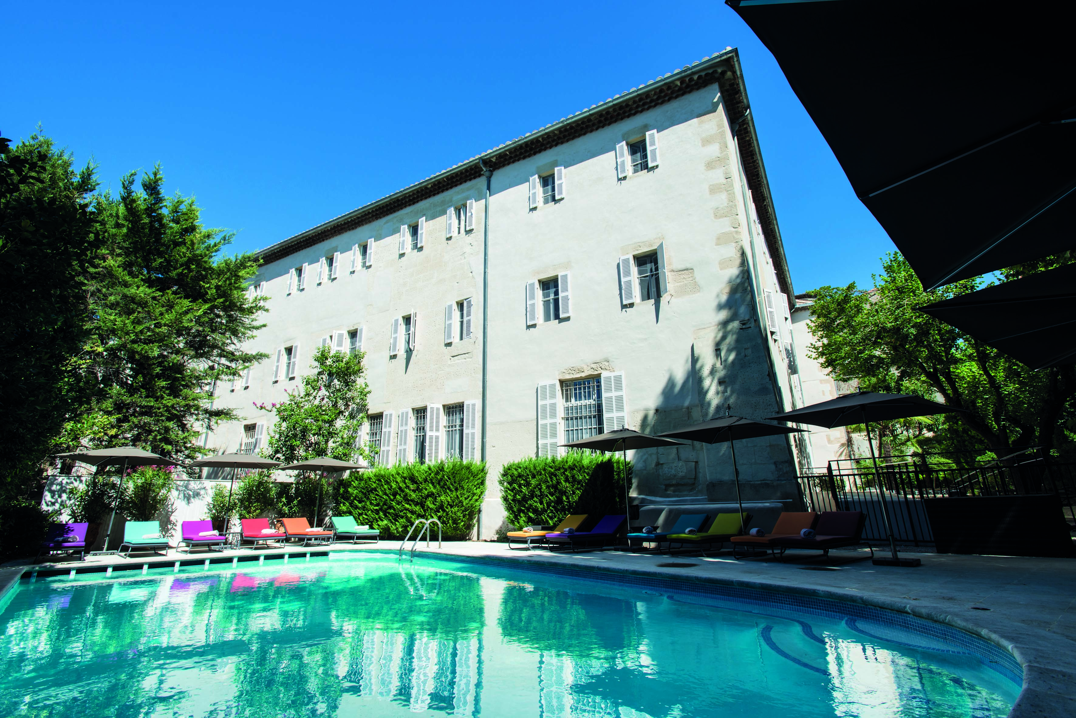 Hotel Jules Cesar Provence outdoor swimming pool with sun loungers and umbrellas overlooked by a white building 