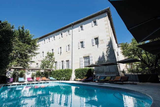 Hotel Jules Cesar Provence outdoor swimming pool with sun loungers and umbrellas overlooked by a white building 