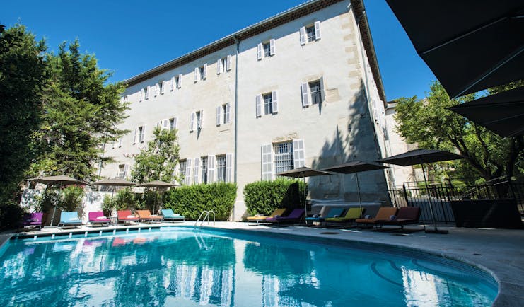 Hotel Jules Cesar Provence outdoor swimming pool with sun loungers and umbrellas overlooked by a white building 