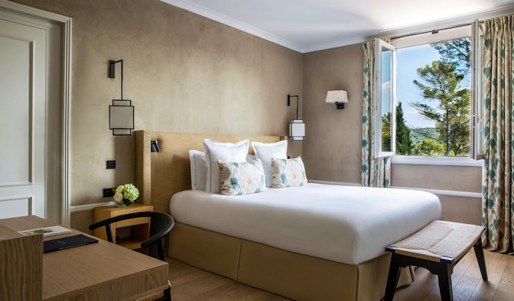 Room with white bed and open window view of trees at le Pigonnet