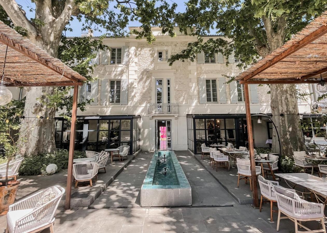 Hotel Le Saint-Remy outdoor dining, with white tables and chairs under rattan canopies and tall trees outside the back of the white-stone hotel building
