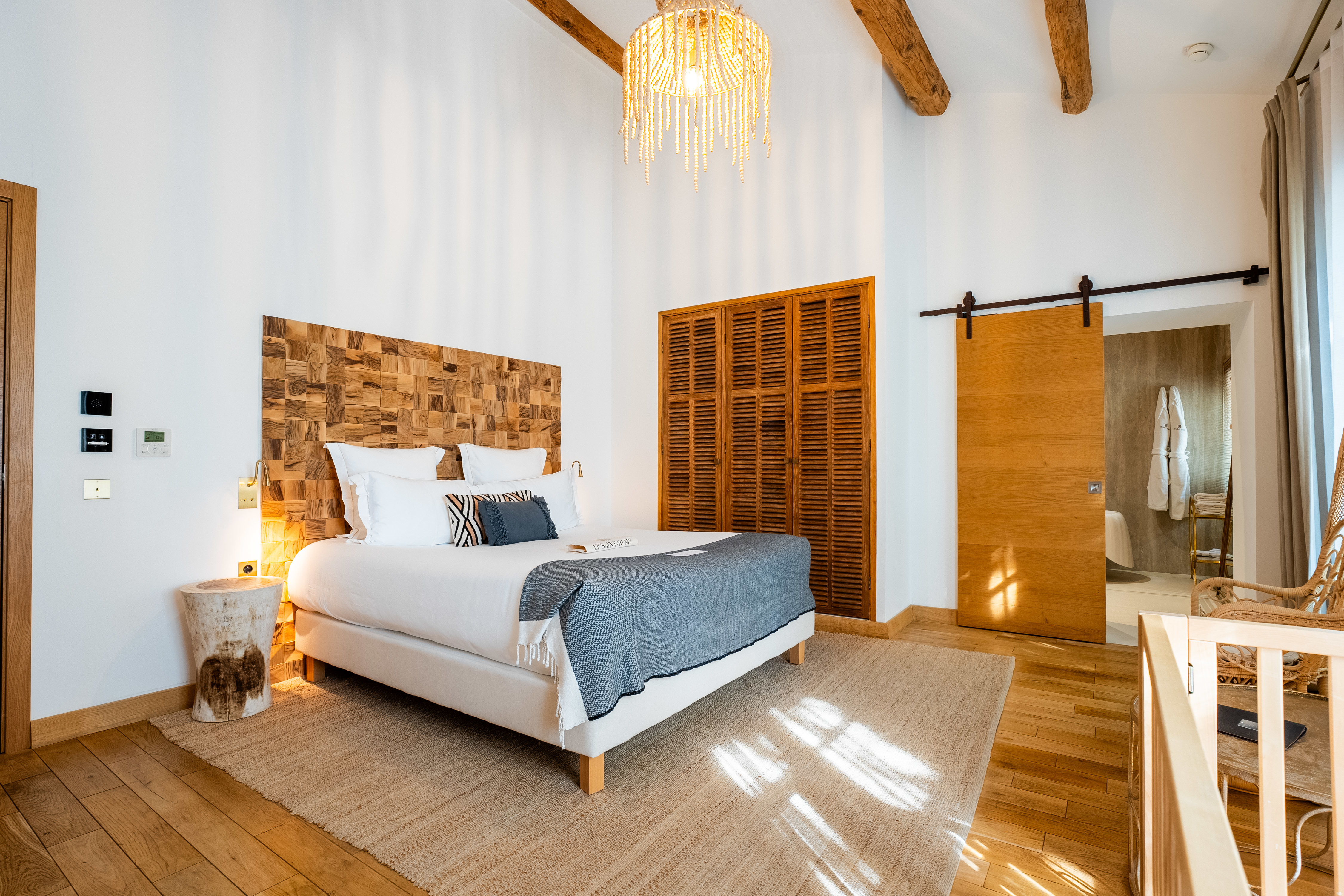 Hotel Le Saint-Remy guest room, with high beamed ceilings, wooden floor, sliding barn-style doors, and large bed with white and blue-grey sheets