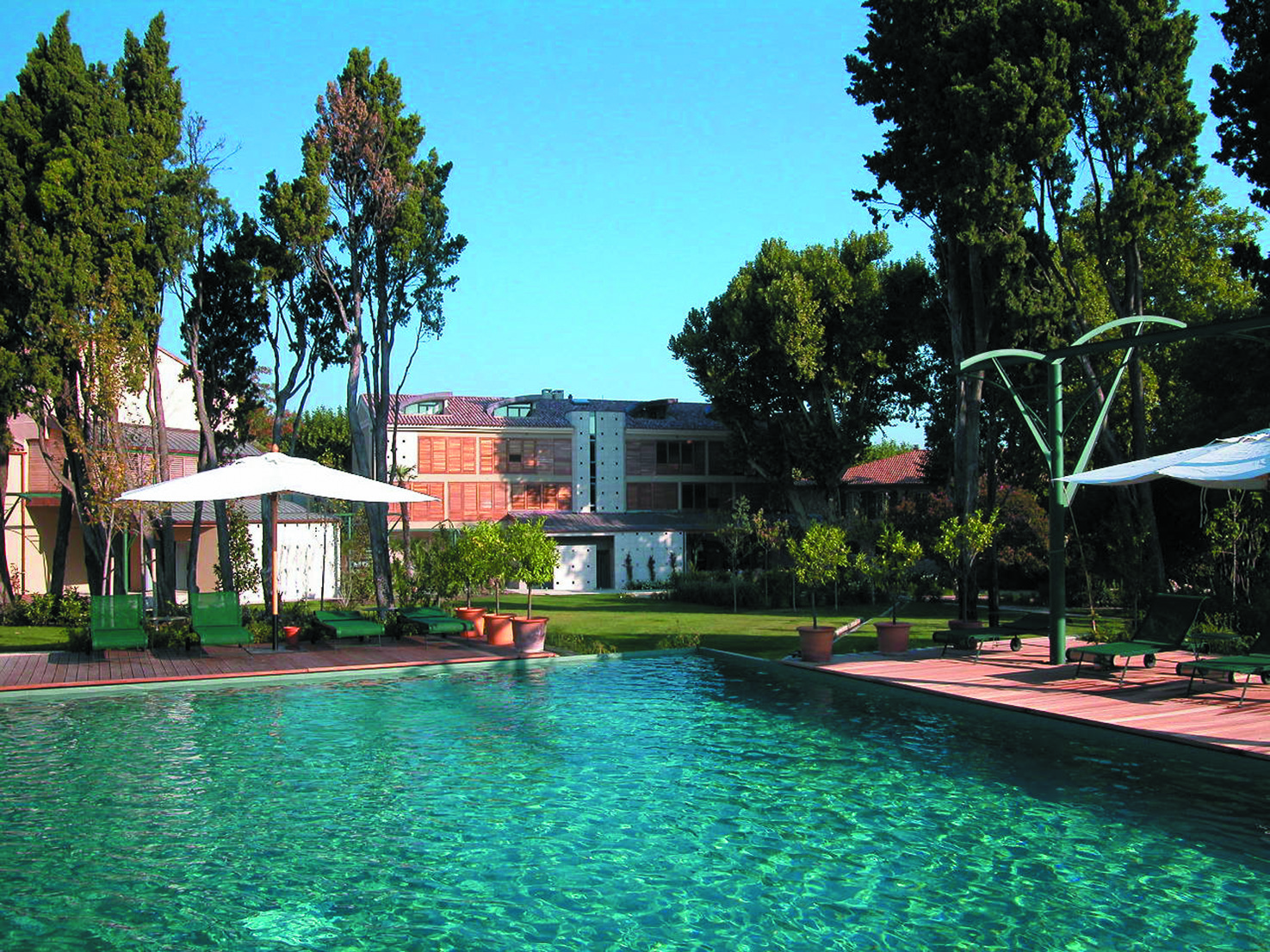 Outdoor pool with loungers and umbrellas and green trees surroudning