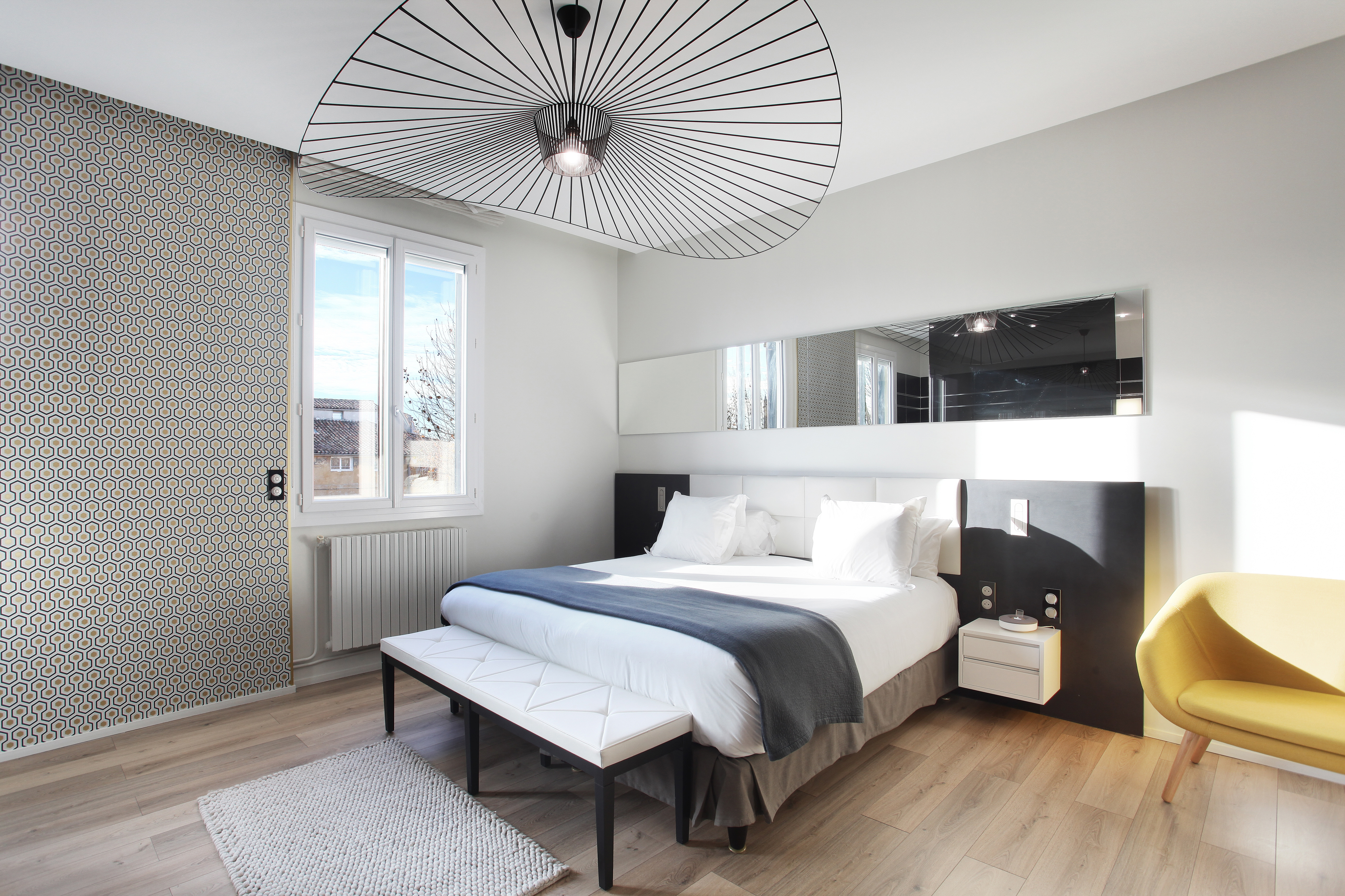 Hotel Negrecoste room, with white and dark grey colour scheme, wooden floors, yellow armchair, and fanning, designer lightshade