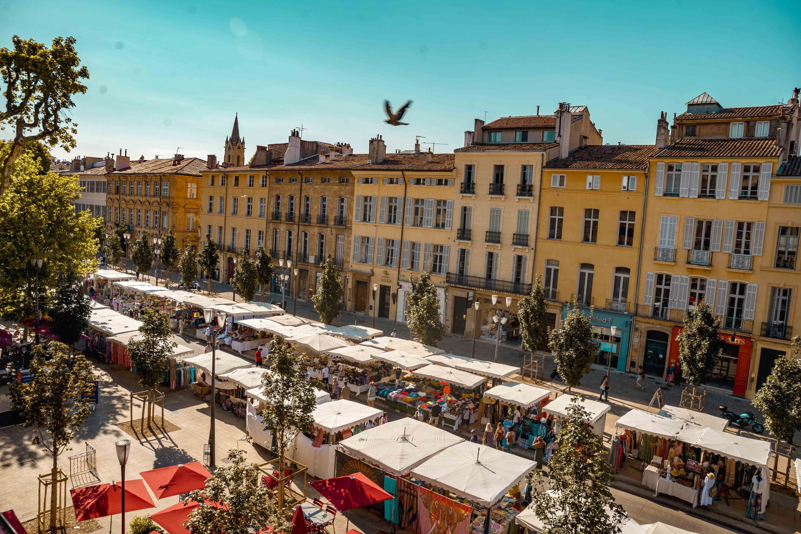 Hotel Negrecoste view out onto the busy Cours Mirabeau, with colourful townhouses, market stalls, and evenly spaced trees