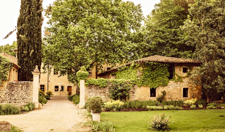 Le Galinier exterior showing driveway leading up to stone building and outhouses, with ivy-cover walls and tall trees