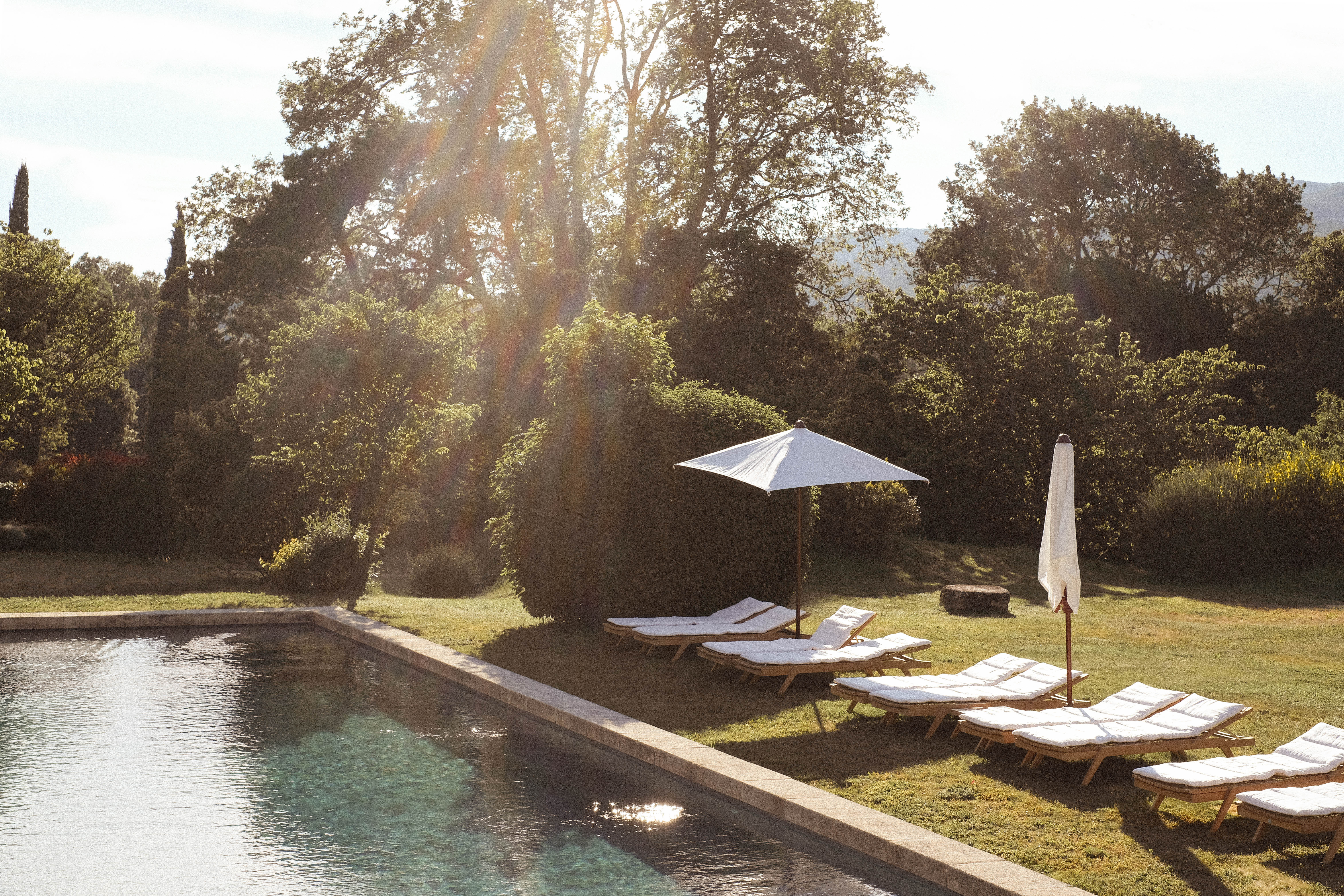 Le Galinier swimming pool lined with white sun loungers and parasols, with trees behind