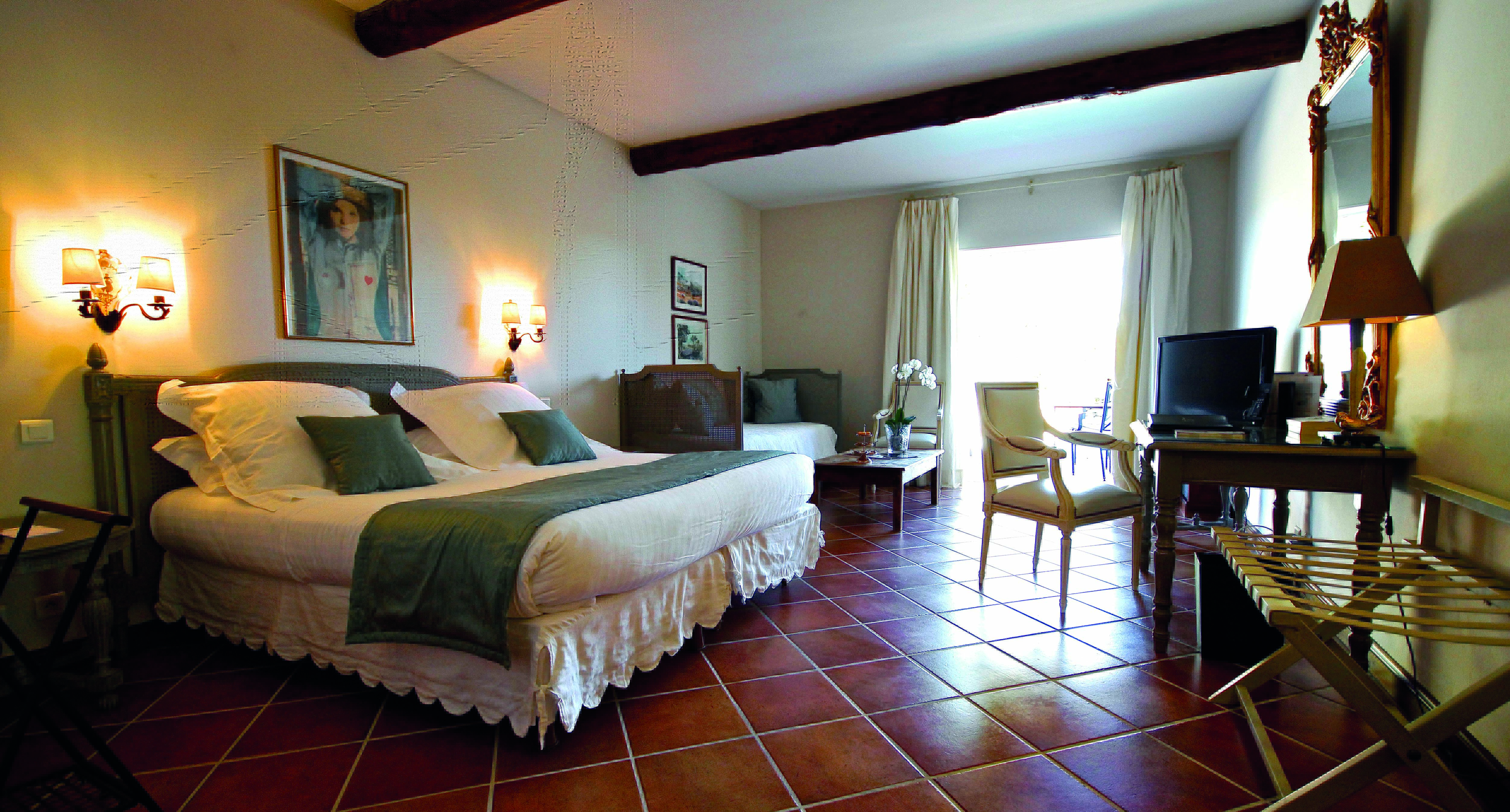 Double room with large double bed, tiled floors, desk, sofa and windows opeing onto a balcony