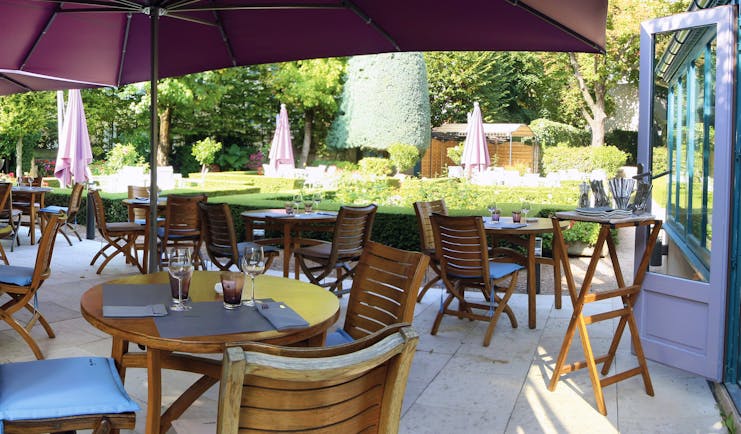 Outdoor terrace seating area with wooden tables and chairs set up around the patio with large purple umbrellas set up