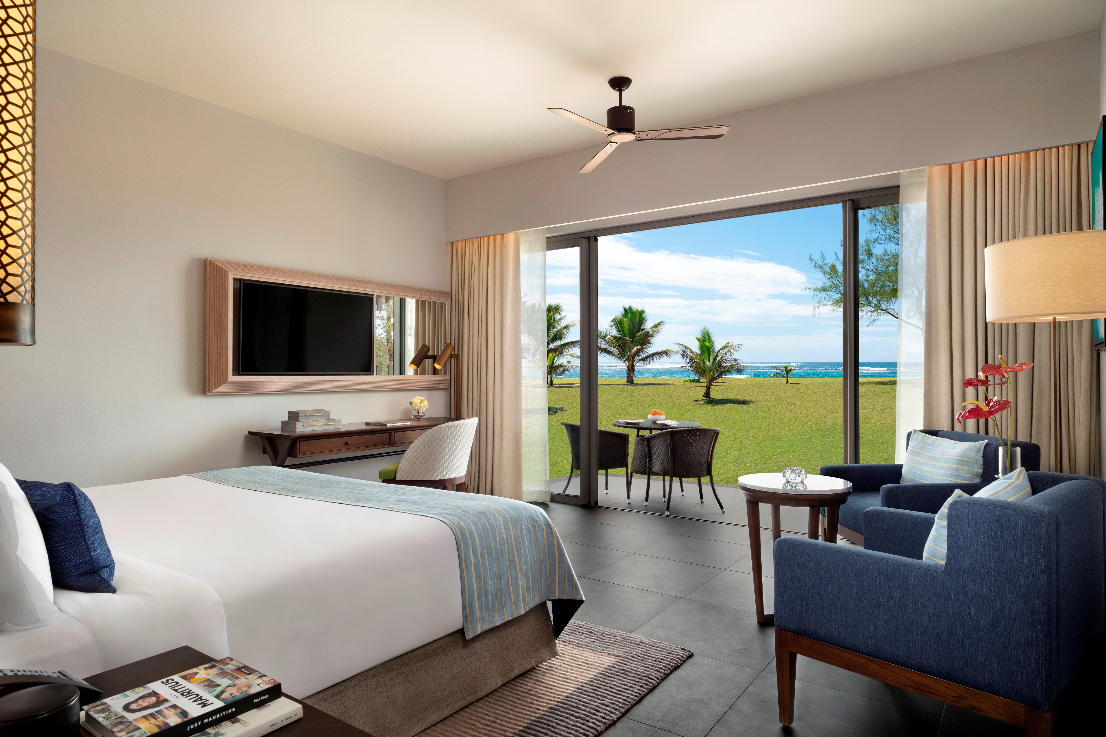 Hotel guest room with double bed, television, arm chair and doors opening onto terrace area 