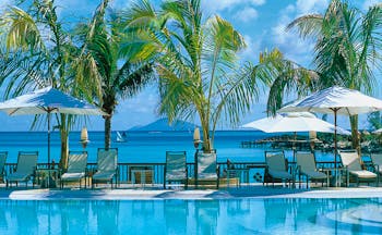 Lux Grand Gaube Mauritius poolside sun loungers umbrellas palm trees ocean in background