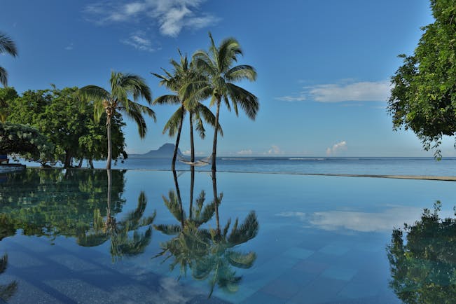 Infinity pool with palm trres reflecting in the water and ocean in the distance