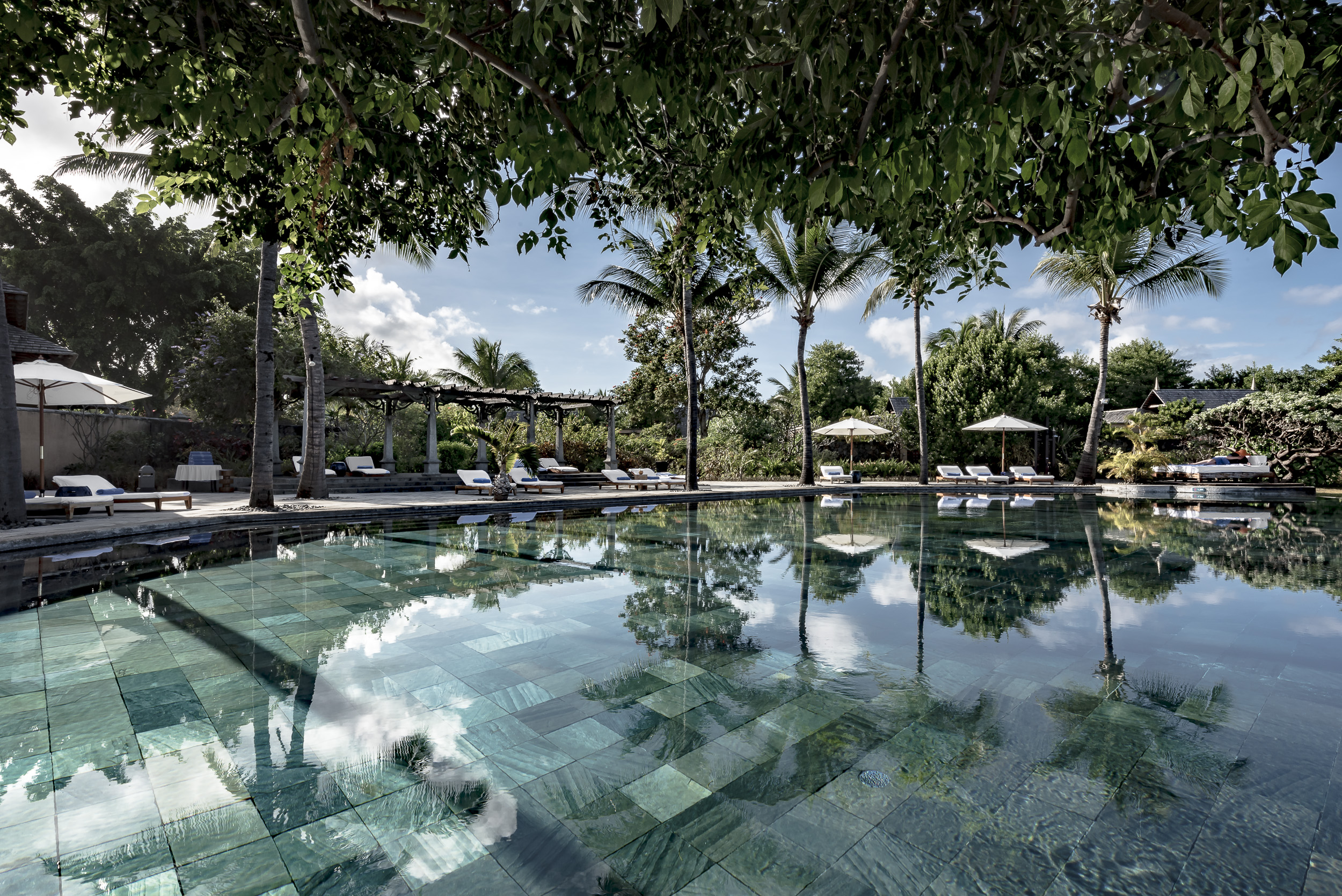 Main pool with sun loungers, umbrellas and palm trees around the outside 