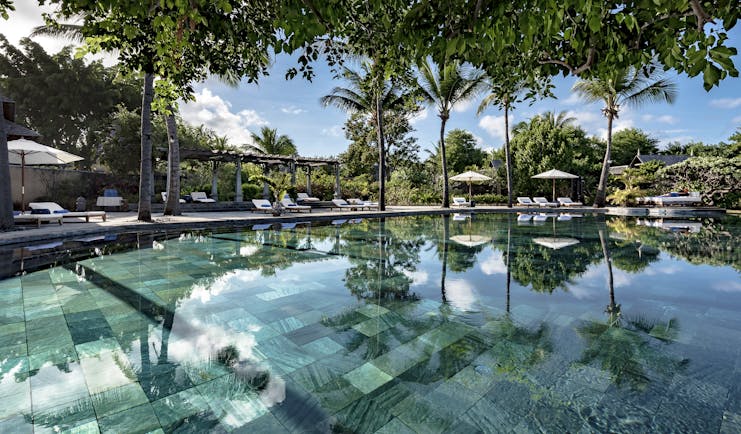 Main pool with sun loungers, umbrellas and palm trees around the outside 