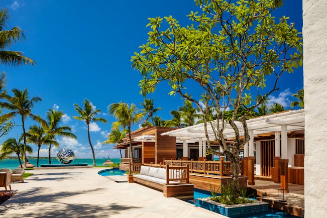 Terrace bar outside with palm trees and sand around and lots of cushioned seating areas