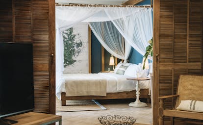 Paradise Cove senior suite, canopied bed, living area with wicker doors, armchairs, television