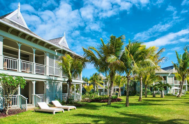 Villa exterior with villa beach style houses opening onto a grassy terrace with palm trees and sun loungers on 