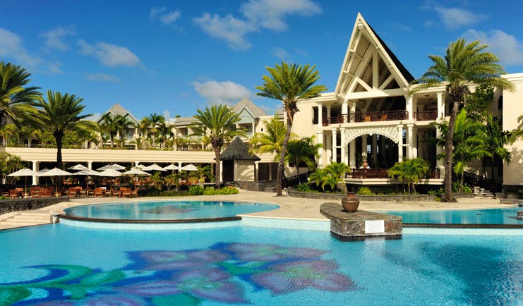 Outside swimming pool with sun loungers, umbrellas and palm trees surrounding it