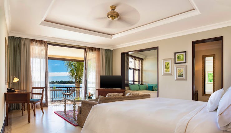 Bedroom with large double bed, electric fan, television, and double doors opening onto balcony looking over sea