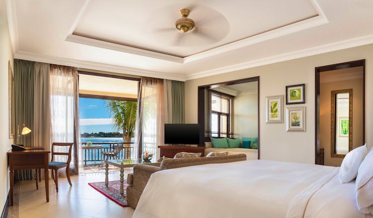 Bedroom with large double bed, electric fan, television, and double doors opening onto balcony looking over sea