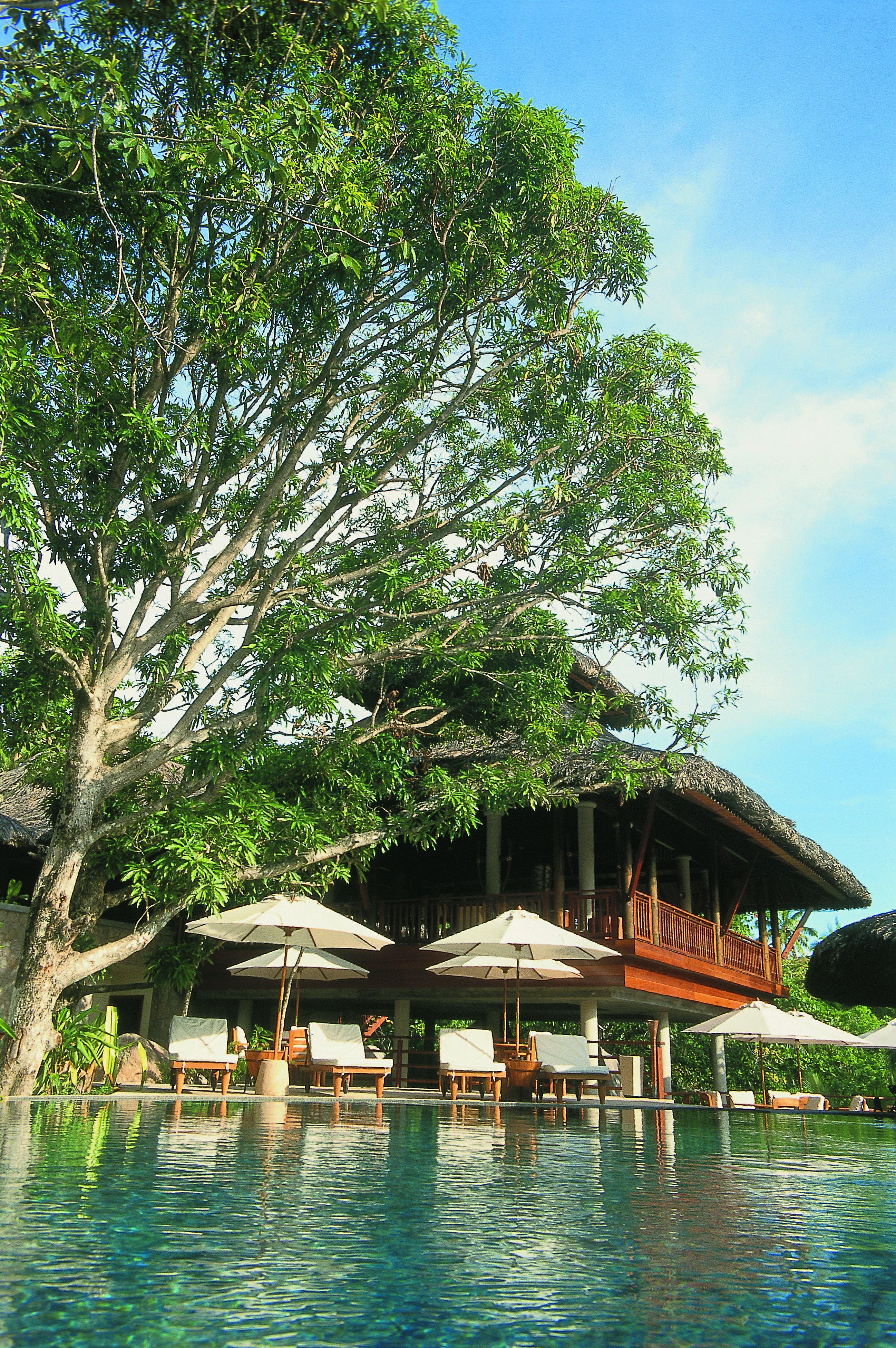 Constance Lemuria Seychelles hotel exterior loungers umbrellas building with deck and thatched roof
