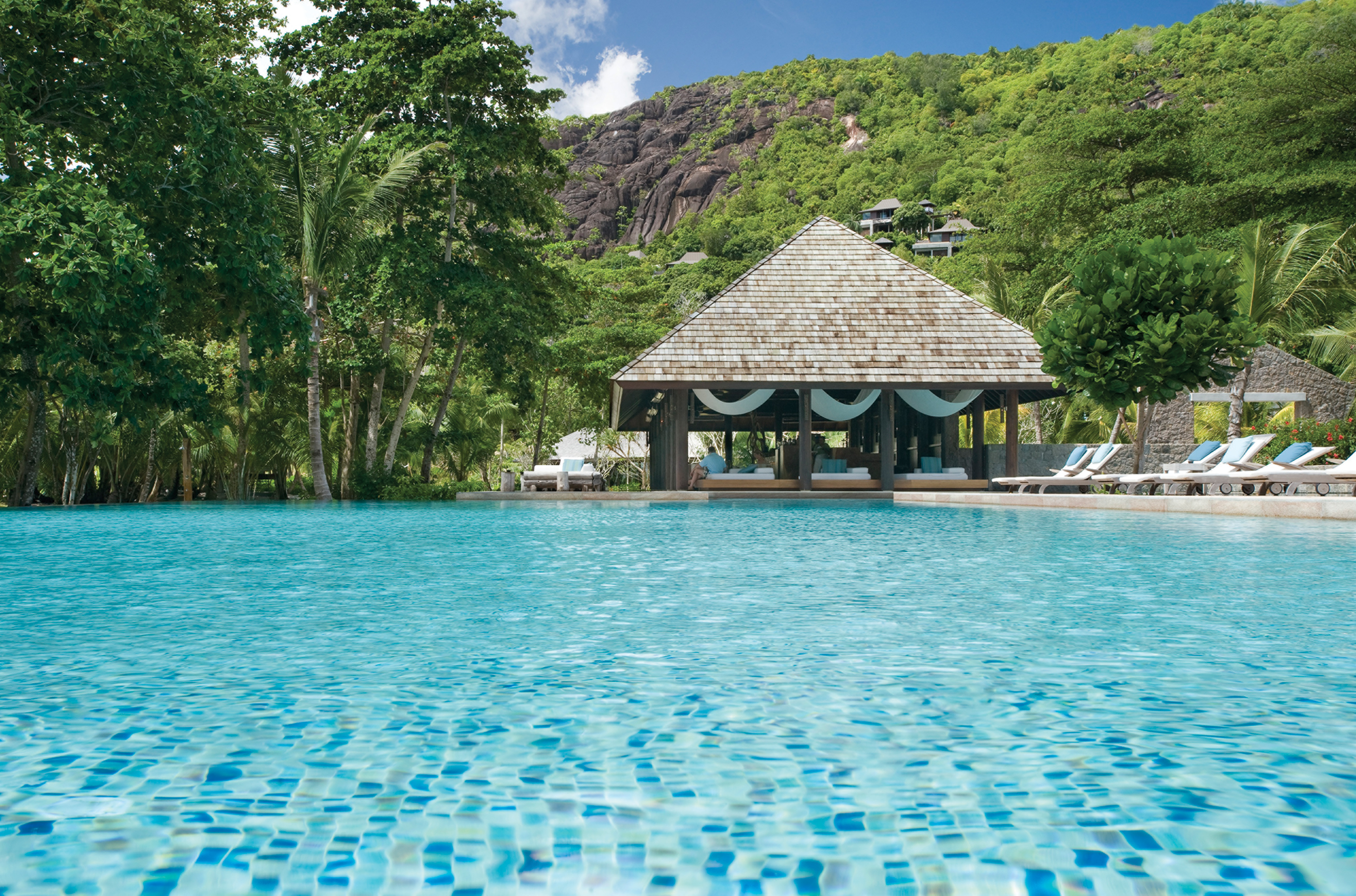 Swimming pool with beach hut in the back ground and sun loungers around the outskirts of the pool