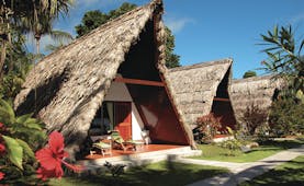 La Digue Island Lodge chalet exterior, triangle shped building, thatched roof, pathway across green lawn to front door
